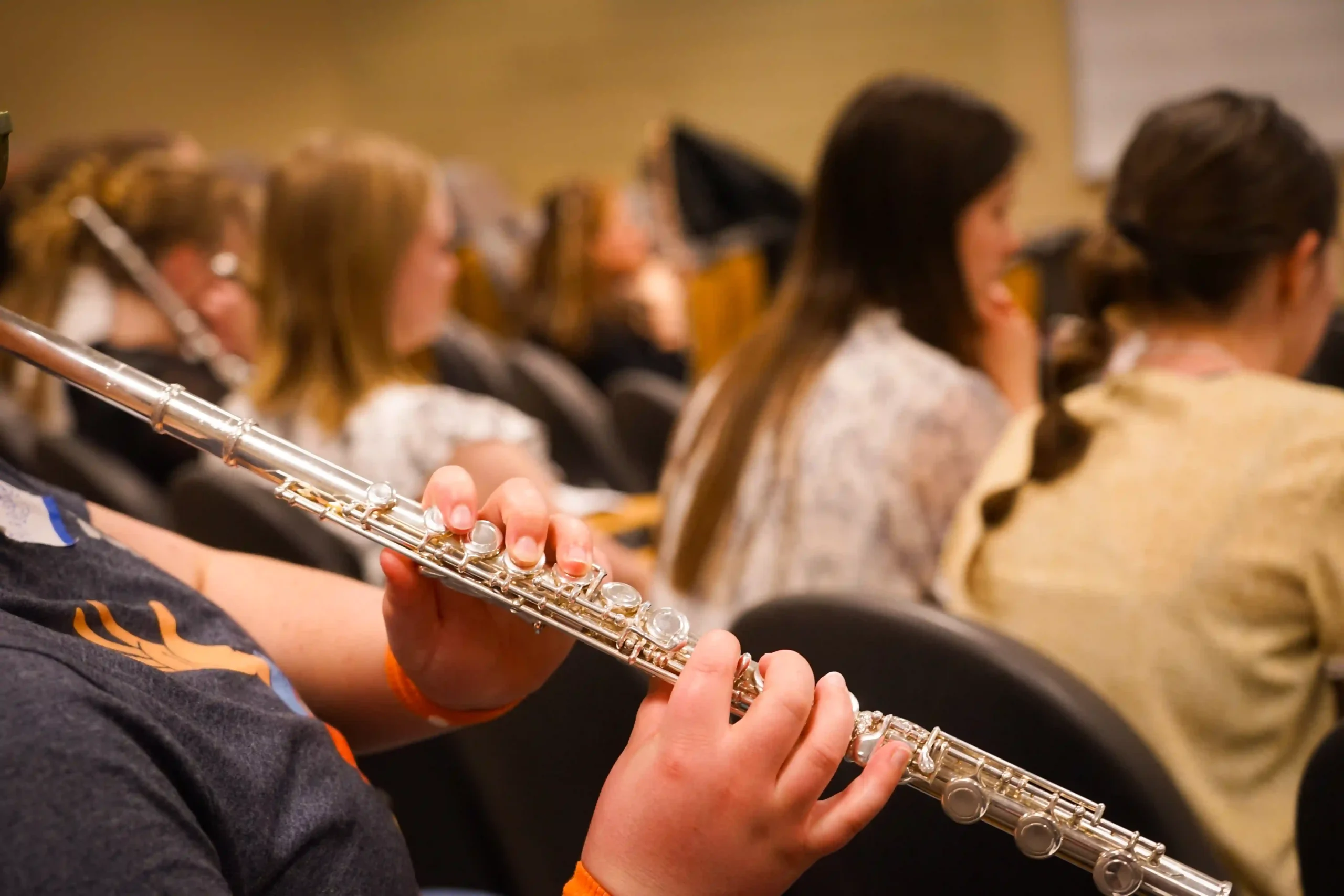 Flutists seated together during a Utah Flute Association session, with one player's hands on a flute in the foreground
