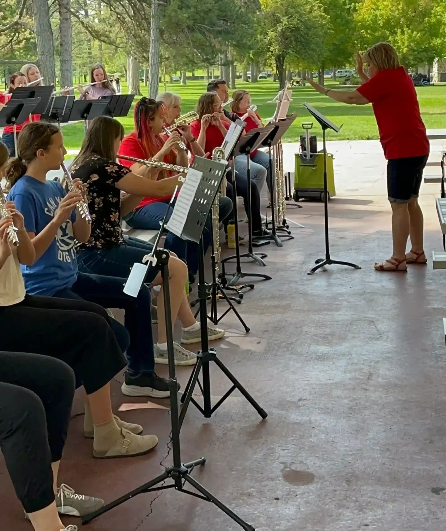 A Utah Flute Association flute choir performing together outdoors under a pavilion, led by a conductor.
